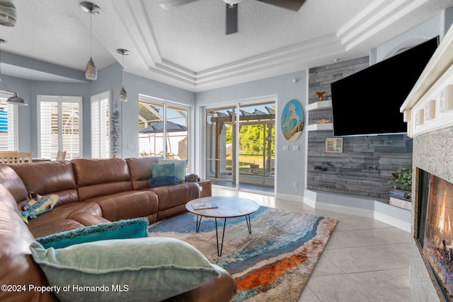 tiled living room with a textured ceiling, a raised ceiling, ceiling fan, and wooden walls