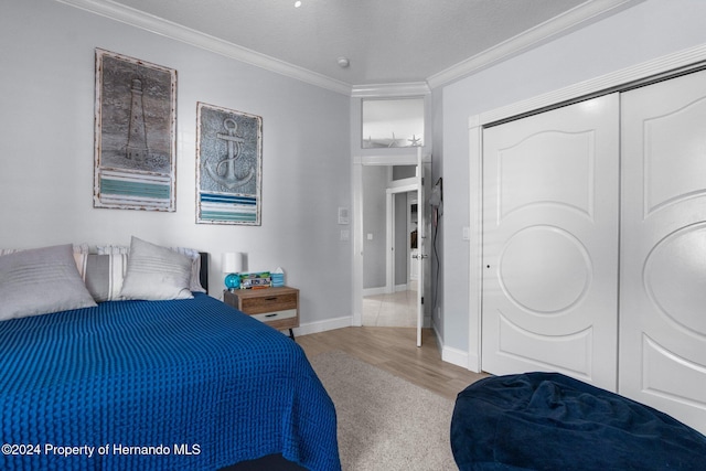 bedroom featuring a textured ceiling, light hardwood / wood-style floors, crown molding, and a closet