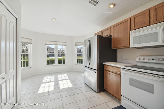 kitchen with a textured ceiling, light tile patterned flooring, and white appliances