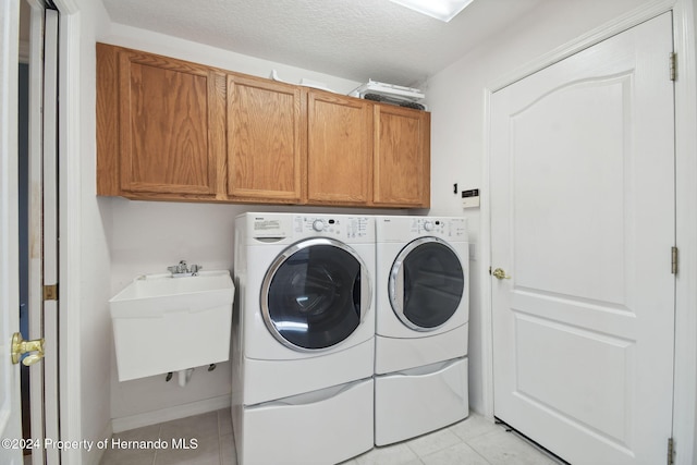 laundry room featuring cabinets, a textured ceiling, sink, washer and dryer, and light tile patterned floors