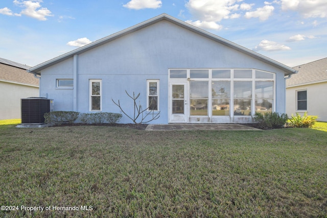 rear view of house with a sunroom, central AC unit, and a lawn