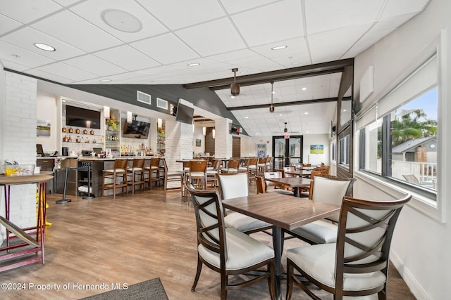 dining area with lofted ceiling with beams, wood-type flooring, and bar