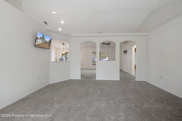 carpeted spare room featuring ceiling fan with notable chandelier and lofted ceiling