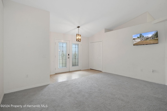 empty room with an inviting chandelier, light colored carpet, french doors, and vaulted ceiling