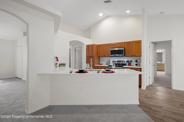 kitchen with light carpet, high vaulted ceiling, tasteful backsplash, kitchen peninsula, and stainless steel appliances