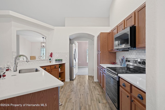 kitchen featuring kitchen peninsula, decorative backsplash, stainless steel appliances, sink, and light hardwood / wood-style flooring