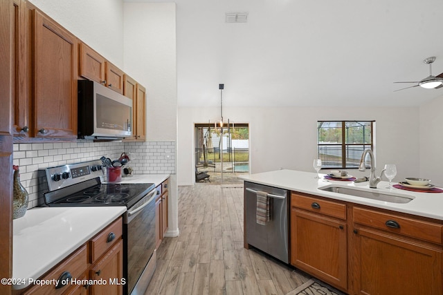 kitchen featuring light wood-type flooring, ceiling fan with notable chandelier, stainless steel appliances, sink, and pendant lighting