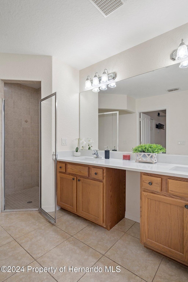 bathroom with tile patterned flooring, vanity, a shower with shower door, and a textured ceiling