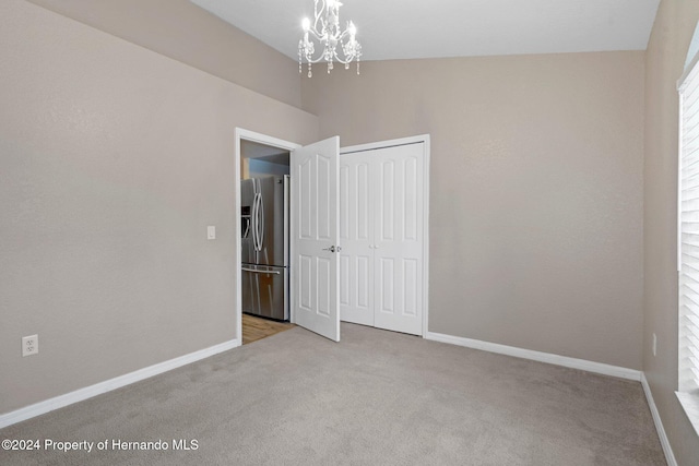 unfurnished bedroom featuring stainless steel fridge, light colored carpet, vaulted ceiling, a notable chandelier, and a closet