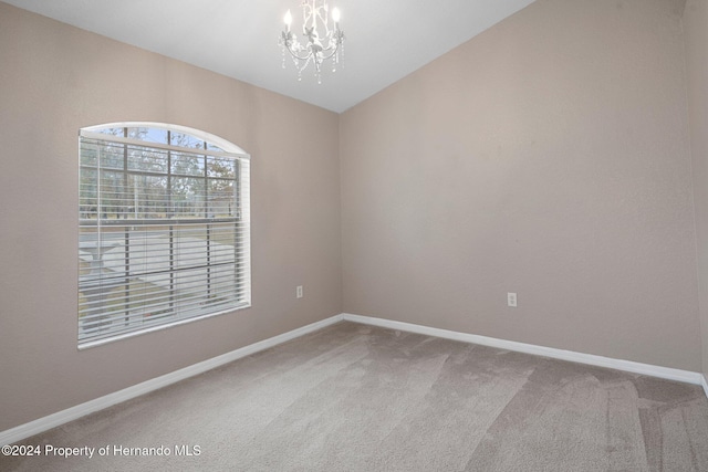 spare room with a chandelier, carpet flooring, and vaulted ceiling