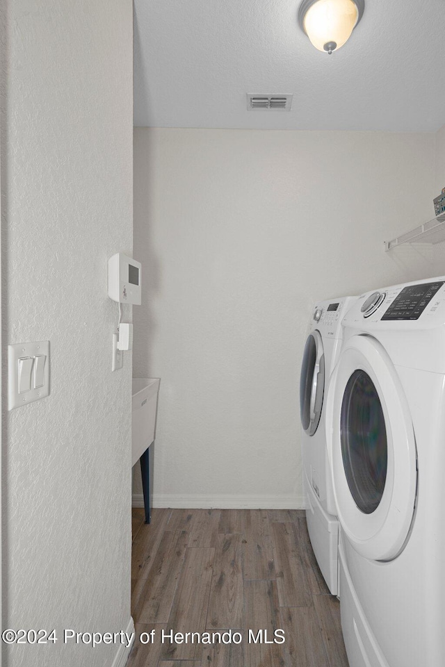 washroom with washing machine and clothes dryer and hardwood / wood-style flooring