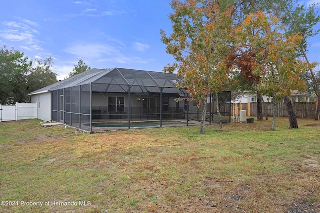 back of property with a fenced in pool, glass enclosure, and a lawn