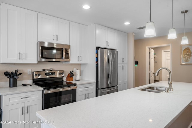 kitchen featuring stainless steel appliances, sink, a center island with sink, white cabinetry, and hanging light fixtures