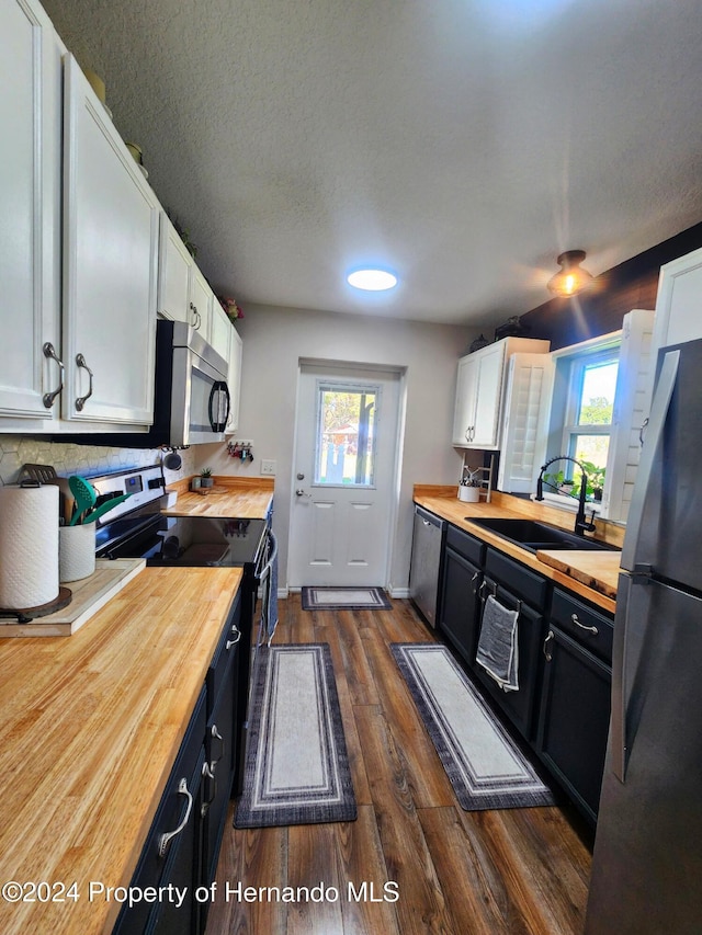 kitchen with stainless steel appliances, white cabinetry, sink, and wooden counters