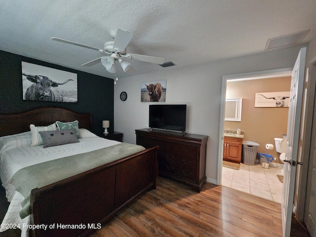 bedroom with ensuite bath, ceiling fan, wood-type flooring, and a textured ceiling