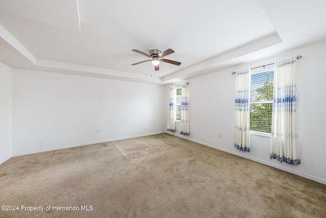 empty room featuring light carpet, a tray ceiling, and ceiling fan