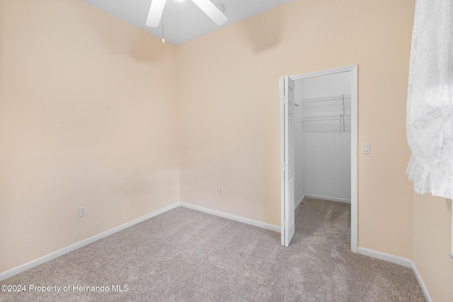 unfurnished bedroom with light carpet, a walk in closet, a closet, and ceiling fan