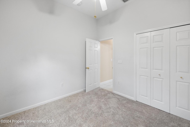 unfurnished bedroom featuring ceiling fan, light carpet, a high ceiling, and a closet