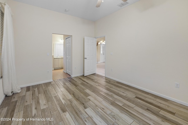 unfurnished bedroom featuring ceiling fan with notable chandelier, light hardwood / wood-style flooring, and connected bathroom