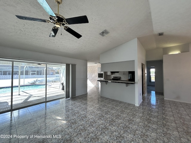 unfurnished living room featuring dark tile patterned flooring, a textured ceiling, vaulted ceiling, and ceiling fan