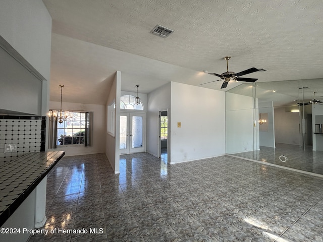 unfurnished living room featuring a textured ceiling, french doors, vaulted ceiling, and ceiling fan with notable chandelier