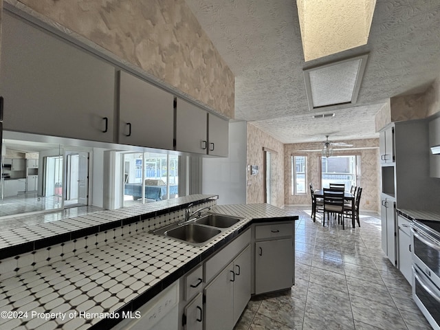 kitchen featuring electric range, sink, ceiling fan, tile countertops, and a textured ceiling