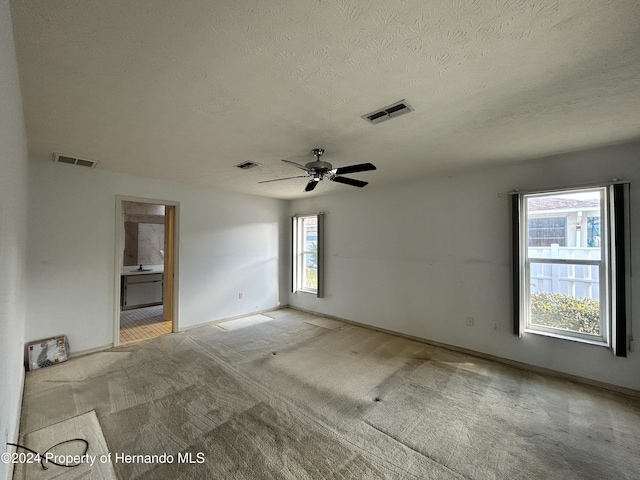 carpeted empty room featuring ceiling fan, plenty of natural light, and a textured ceiling