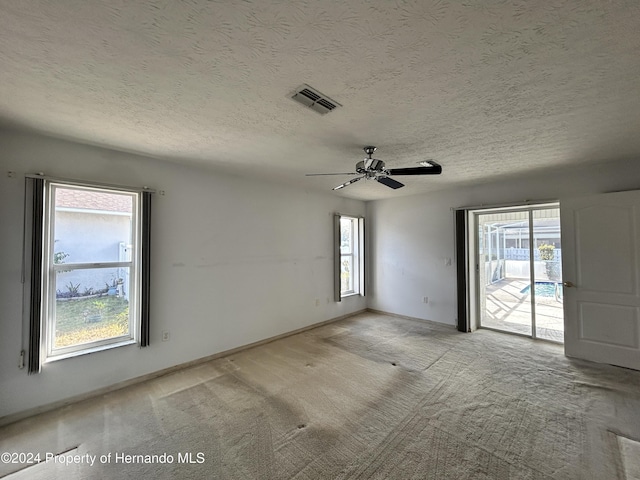 spare room with a textured ceiling, light colored carpet, a wealth of natural light, and ceiling fan