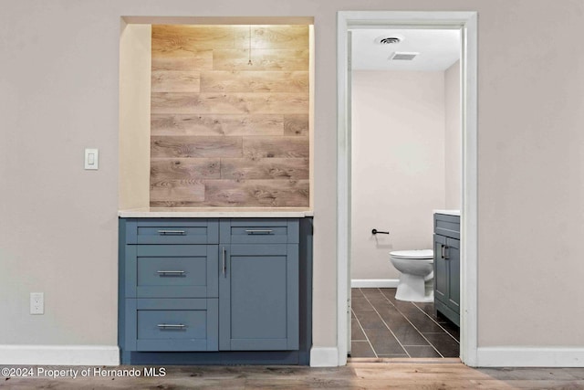 bathroom featuring wood walls, vanity, wood-type flooring, and toilet