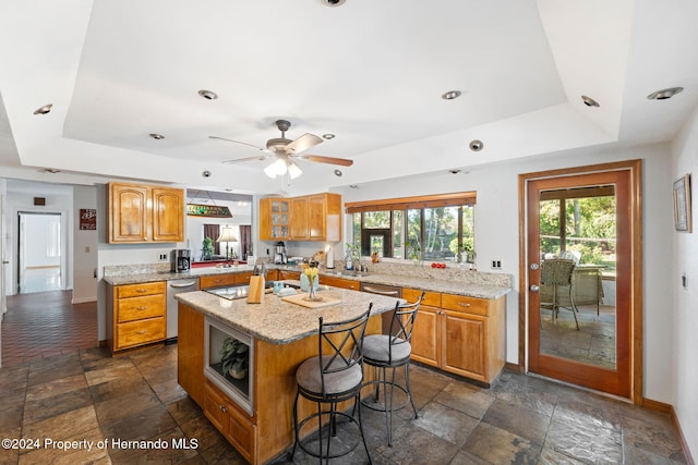 kitchen with a kitchen breakfast bar, a tray ceiling, ceiling fan, dishwasher, and a center island