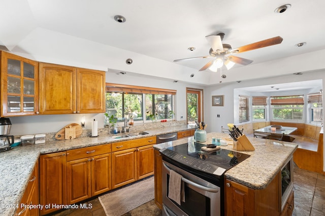 kitchen with a wealth of natural light, light stone counters, sink, and appliances with stainless steel finishes