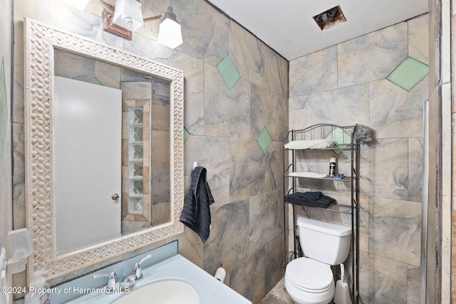 bathroom featuring vanity, toilet, and tile walls