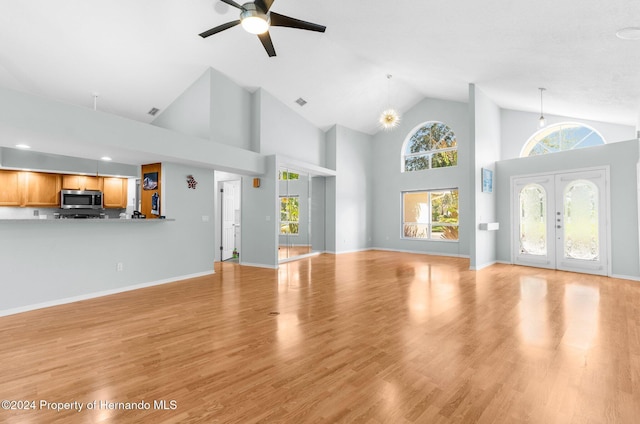 unfurnished living room with ceiling fan, french doors, high vaulted ceiling, and light wood-type flooring