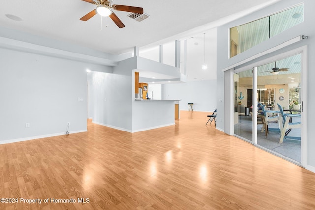 unfurnished living room with ceiling fan, light hardwood / wood-style floors, and a towering ceiling