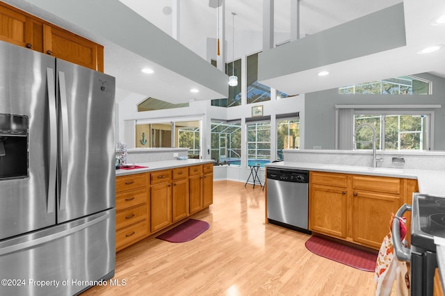 kitchen with high vaulted ceiling, light wood-type flooring, sink, and appliances with stainless steel finishes