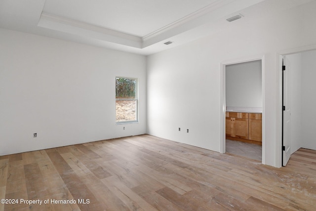 unfurnished room with a raised ceiling, light hardwood / wood-style floors, and ornamental molding