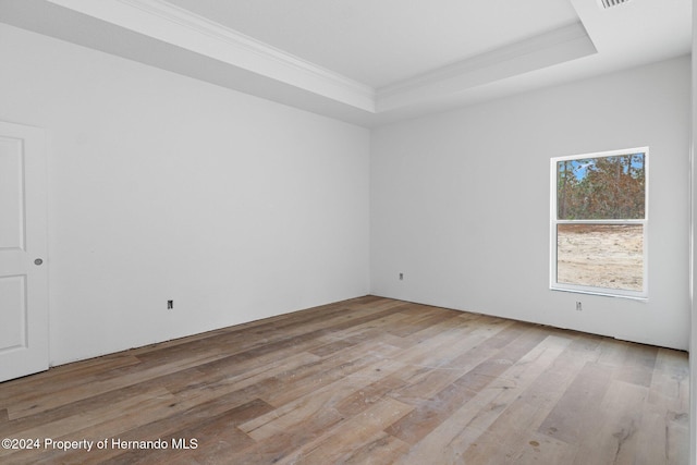 unfurnished room with a tray ceiling, light hardwood / wood-style floors, and ornamental molding