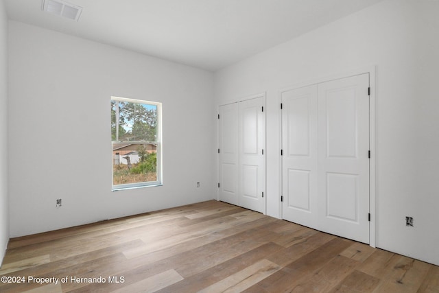 unfurnished bedroom featuring two closets and light wood-type flooring