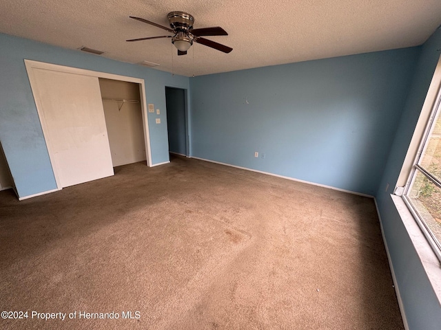 unfurnished bedroom with dark colored carpet, ceiling fan, a textured ceiling, and a closet