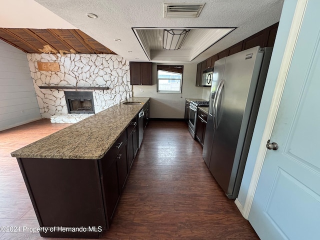 kitchen featuring dark brown cabinetry, a stone fireplace, a textured ceiling, appliances with stainless steel finishes, and hardwood / wood-style flooring