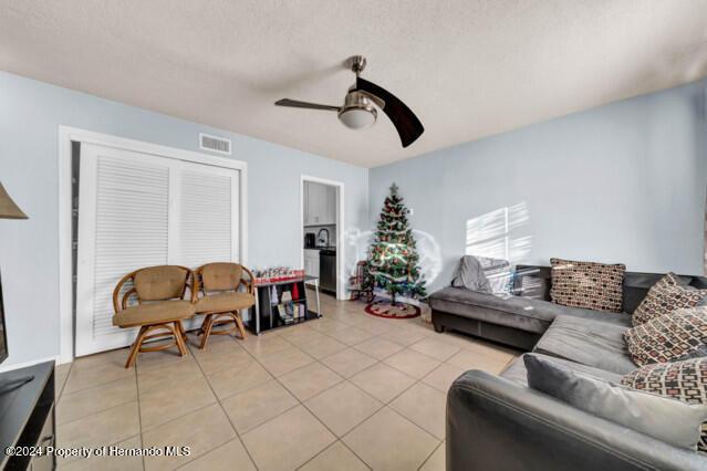 tiled living room with ceiling fan and a textured ceiling