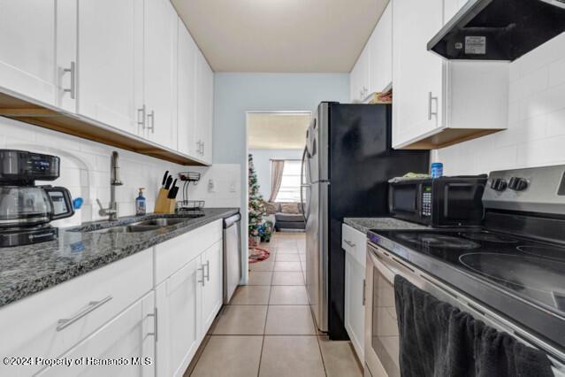 kitchen featuring stainless steel appliances, sink, light tile patterned floors, white cabinets, and range hood