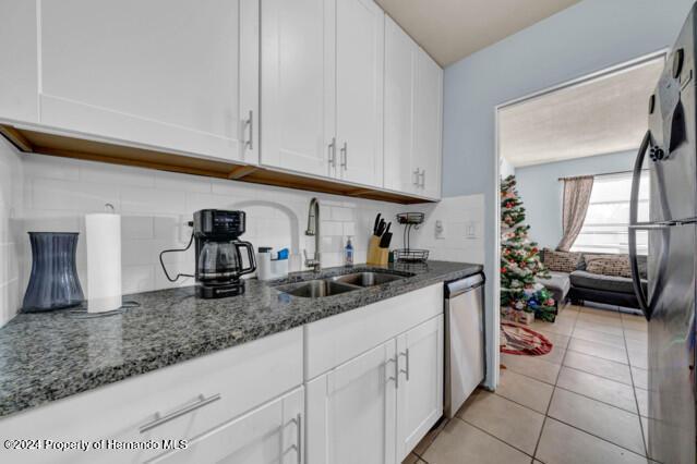 kitchen with sink, white cabinets, dark stone counters, light tile patterned flooring, and appliances with stainless steel finishes