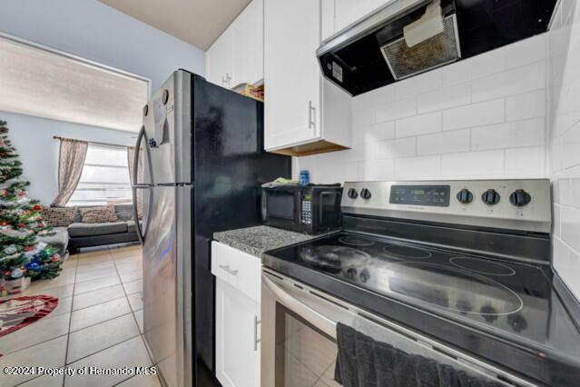 kitchen featuring decorative backsplash, light tile patterned floors, appliances with stainless steel finishes, white cabinetry, and extractor fan