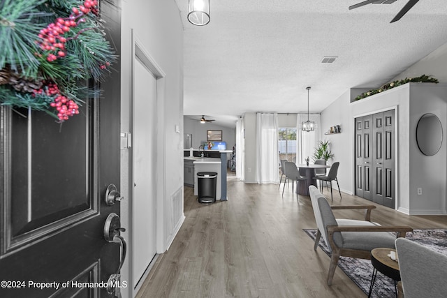 foyer entrance featuring a textured ceiling, ceiling fan with notable chandelier, hardwood / wood-style flooring, and lofted ceiling