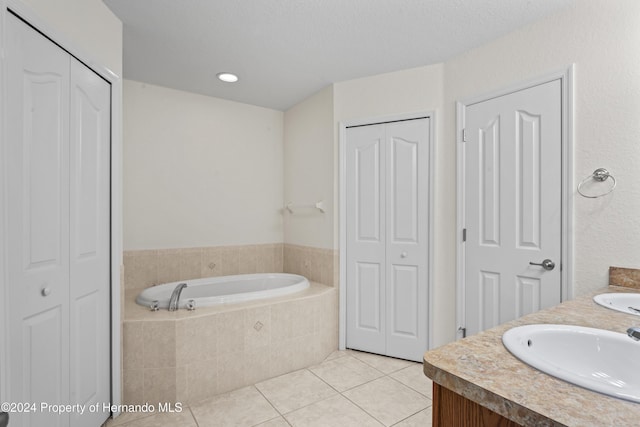 bathroom with a textured ceiling, vanity, tiled bath, and tile patterned floors