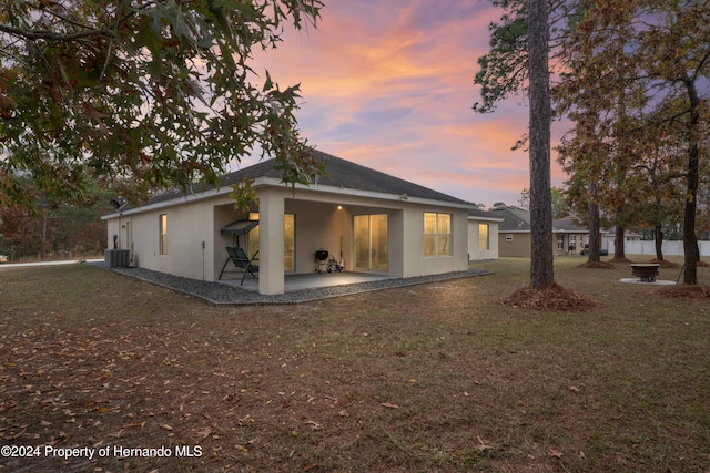 back house at dusk with a yard, a patio, and central air condition unit