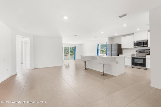 kitchen featuring white cabinets, a breakfast bar area, light tile patterned floors, a kitchen island, and stainless steel appliances