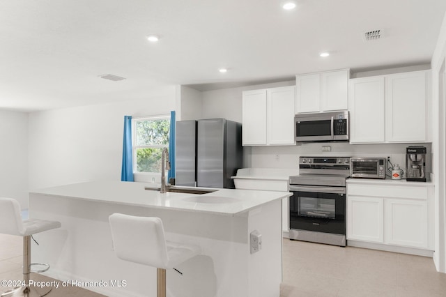 kitchen with white cabinetry, a kitchen island with sink, a breakfast bar, and appliances with stainless steel finishes