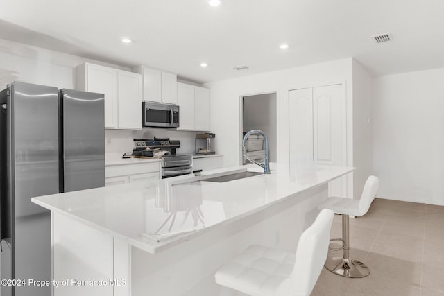 kitchen with appliances with stainless steel finishes, white cabinetry, a large island with sink, and a kitchen breakfast bar